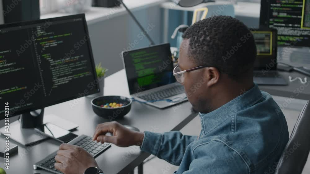 Wall mural chest up of young black man in eyeglasses and denim shirt program coding on desktop computer while w