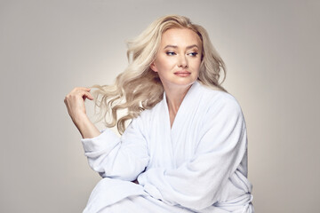 Beautiful dreaming mature blonde woman having clean skin in housecoat over a grey isolated...