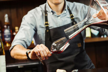 Sommelier pouring wine into glass from mixing bowl. Male waiter