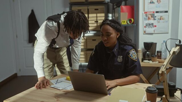 Man and woman officers review case files on a laptop in a police station with missing persons posters in the background