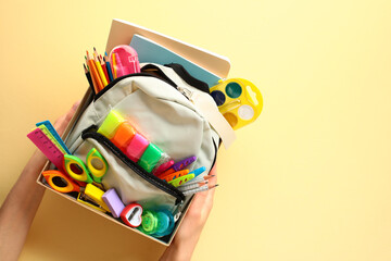 Top view of donation box with backpack filled with vibrant school supplies in womens hands on a...
