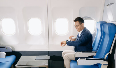 Attractive Asian male passenger of airplane sitting in comfortable seat while working laptop and...