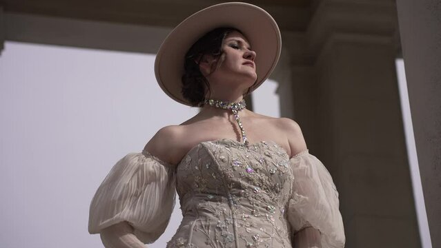 Elegant woman in vintage dress by classical columns, showcasing timeless fashion and grace