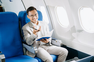 Young Asian executive excels in first class, multitasking with digital tablet, laptop and...