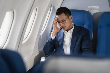 Tired asian man with headache feeling sick while sitting in the airplane , Passengers near the window.