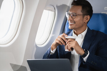 Asian businessman enjoying enjoys a coffee comfortable flight while sitting in the airplane cabin,...