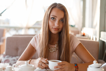 beautiful girl in a fashionable dress sits in a cafe and drinks tea outdoors