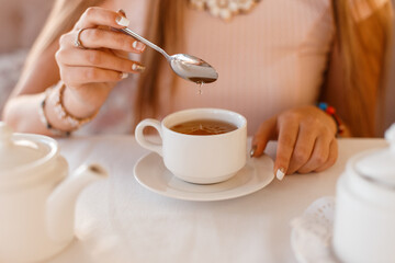 Pretty girl holds a spoon and stirs tea, close-up. Woman drinking tea
