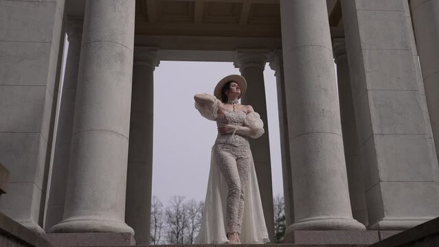 Picture of an elegant woman in a Victorian dress striking a pose next to columns