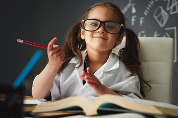 Portrait, preschooler and classroom with books, pencil and learning in education for childhood...