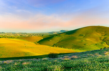 spring or summer beautiful landscape of green hills and flowering meadow with fields and mountains and amazing cloudy sunset sky on backgeound
