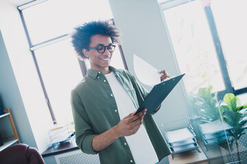 Photo of cheerful handsome agent dressed khaki shirt eyewear reading documents signing papers...