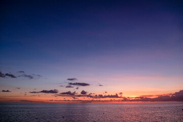 A tranquil seascape at sunset with vibrant orange and purple hues painting the sky and gentle waves on the water surface.