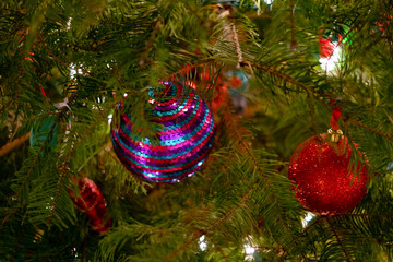 Close-up of Christmas tree branches adorned with a shiny blue and a glittering red bauble, illuminated by twinkling festive lights.
