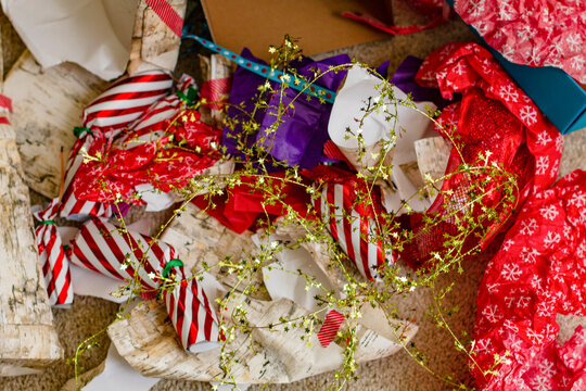 A cluttered arrangement of colorful Christmas gift wrapping paper, ribbons, and bows scattered on the floor, indicating a recent unwrapping session.