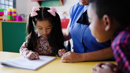 Teacher helping kid students learn to read in classroom at kindergarten school room. Multiracial and education concept - Powered by Adobe