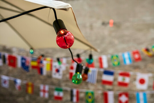 Colored light bulbs are strung in front of a blurred background featuring small international flags hung across a cord.