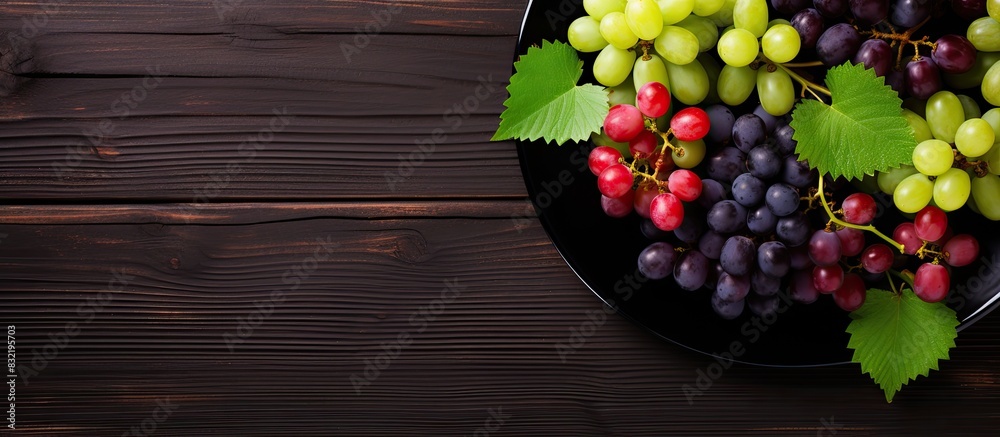 Poster top view of various types of grapes on vintage plate on black wooden surface. creative banner. copys
