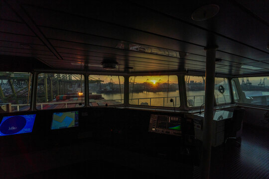 Sunrise viewed through the window of a ship's bridge with navigational equipment visible.