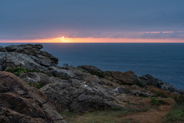 sunset over the ocean with rocks in the foreground and dramatic purple covered sky