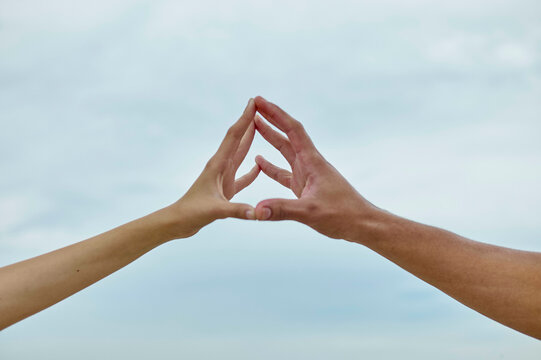 Two hands are forming a triangular shape against a cloudy sky backdrop.