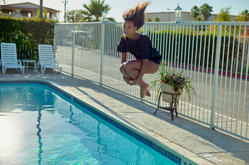 A child is captured mid-jump into a swimming pool, with their hair flipping upwards and a focused expression on their face.