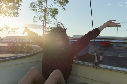A joyful person spreads their arms wide, embracing the wind with their hair blowing, as they ride in a boat at sunset.