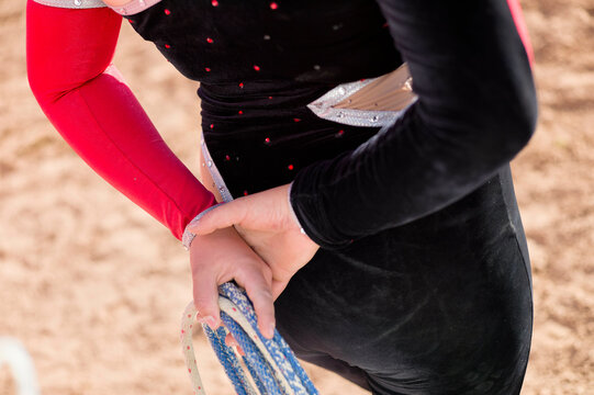 A close-up of an individual in a black and red costume with silver accents adjusting their blue and silver figure skating blade cover.