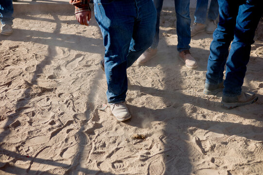 A group of people walking on sandy ground, captured focusing on their lower bodies and footsteps.