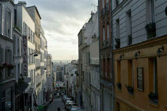 A view of a narrow European street lined with traditional buildings featuring a restaurant sign, under a cloudy sky.