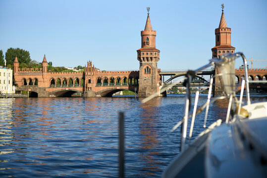 The image shows the Oberbaum Bridge spanning across the Spree River in Berlin viewed from the perspective of a boat's bow.