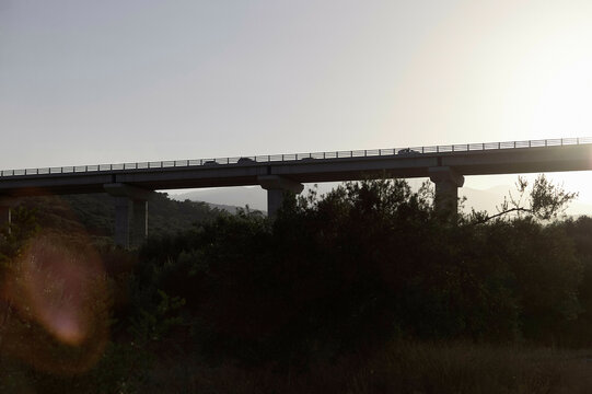 A bridge spans across the frame amidst a natural landscape, illuminated by the soft light of the setting or rising sun.