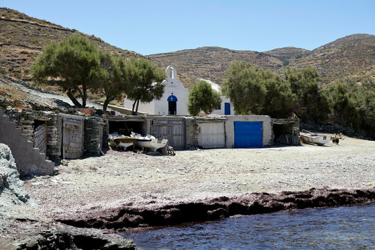 A serene coastal scene featuring a small white church with a blue dome, set against a hilly landscape with surrounding shrubbery