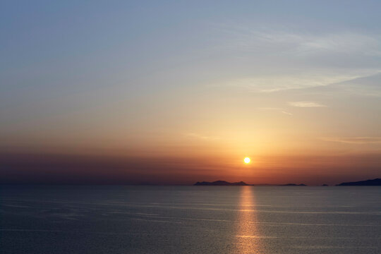 Sunset over a calm sea with islands silhouetted against the sky. - Powered by Adobe