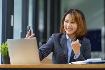 Young pretty Asian businesswomen look at smartphones excited and thrilled with the business success while working at the office.