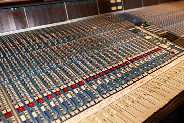 An angled view of a large multi-channel mixing console with numerous sliders, knobs, and buttons, commonly used in audio production for music, television, or film.