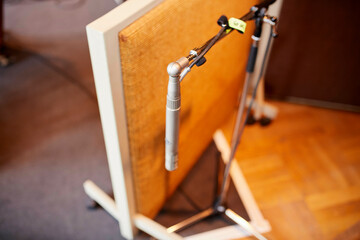 A close-up image of a silver microphone set up in front of a beige speaker cabinet on a wooden floor, with selective focus and blurred background.