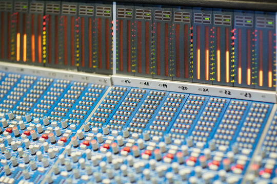 A close-up view of a professional audio mixing console with illuminated level meters displaying sound levels.