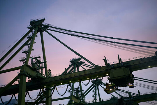 The image captures towering port container cranes against a twilight sky, showcasing the silhouette of the industrial structures.