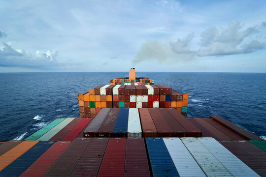 A cargo ship at sea is filled with numerous stacked containers under a cloudy sky, with waves gently lapping at its sides.