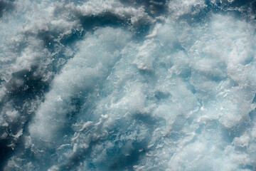 Churning azure waters creating a frothy white texture, showcasing the dynamic movements of the sea.