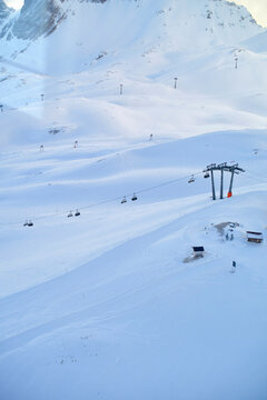 A serene, snow-covered mountain landscape with a ski lift running up the slope and skiers dotting the trails beneath a clear blue sky.