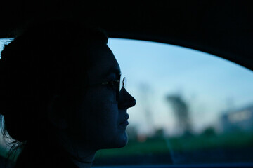 The image displays a profile view of a person sitting inside a vehicle during twilight with a blurred background.