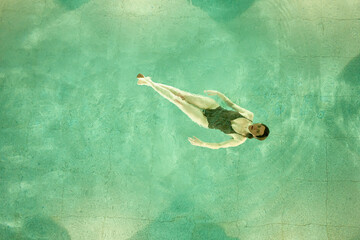 An individual is floating peacefully in clear blue pool water, viewed from above with a serene expression.