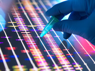 Genomic Research, Scientist holding a DNA sample in a vial with the profile results on screen in the lab