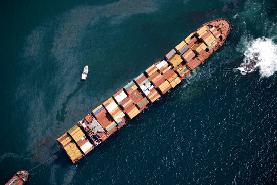 An aerial view of a large cargo ship in trouble at sea, being accompanied by several smaller vessels, New Zealand