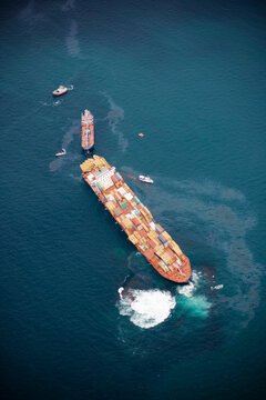An aerial view of a large cargo ship in trouble at sea, being accompanied by several smaller vessels.