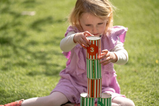 A young child is playing outside on grass, stacking colorful cans with numbers on them.