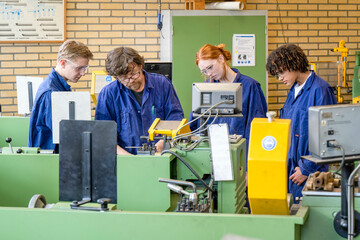 Four people in blue work uniforms are attentively operating and observing machinery in an industrial workshop setting.