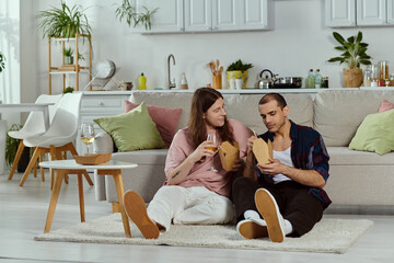 A gay couple relaxes on a couch, enjoying a meal together at home, creating a cozy and intimate...